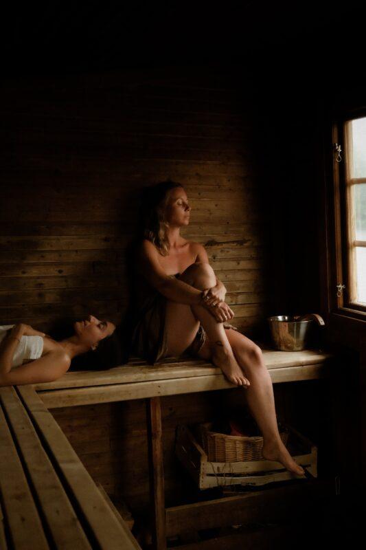 A woman resting with her knees drawn up in a wood-panelled sauna, another guest lying on the bench below