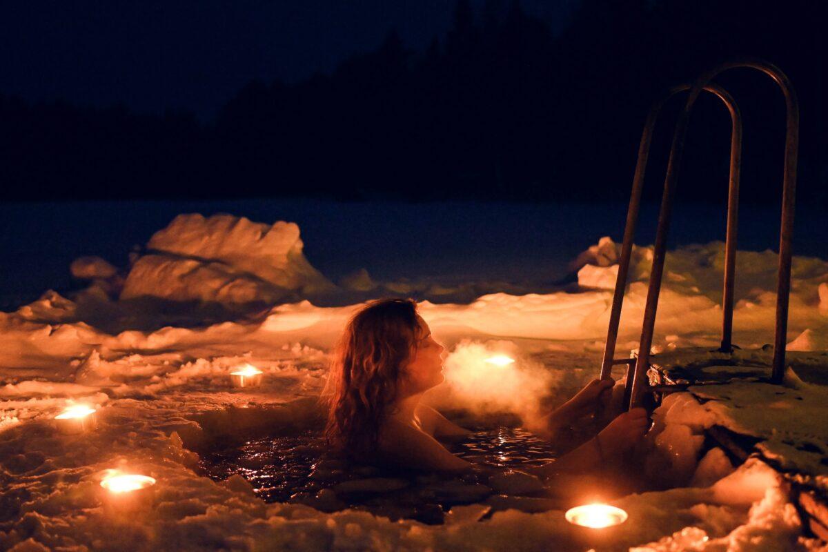 Woman relaxing in a candlelit ice bath surrounded by snow during a winter wellness experience