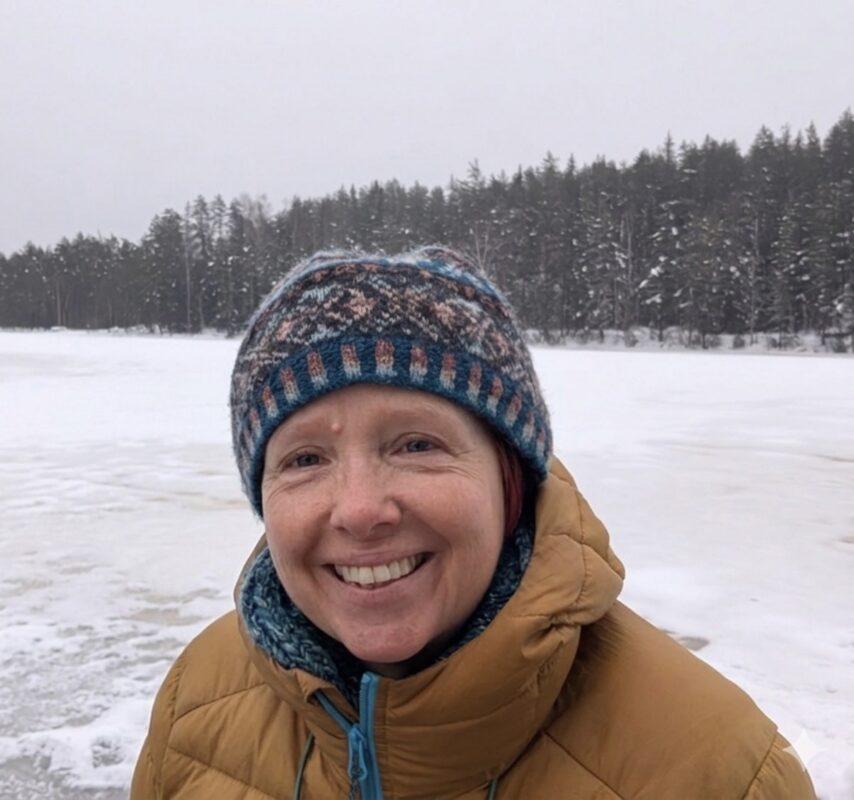 Portrait of Gail smiling outdoors beside a frozen lake during a winter wellness and cold therapy retreat
