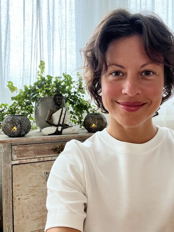 Portrait of yoga teacher Isabella smiling indoors beside plants.