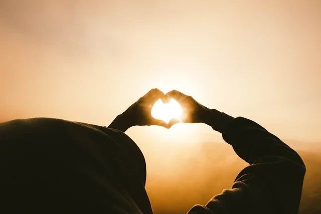 Hands forming a heart shape around the setting sun.
