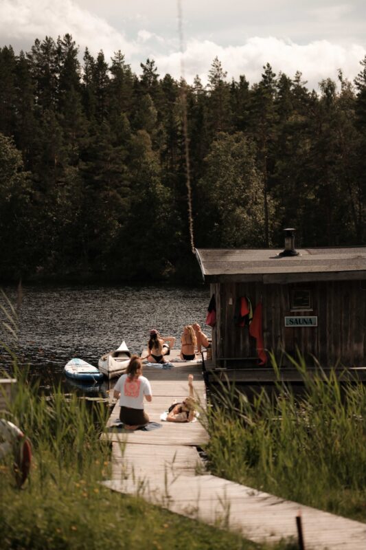Retreat guests relaxing on the dock beside a floating sauna, enjoying the lakeside surrounded by forest.